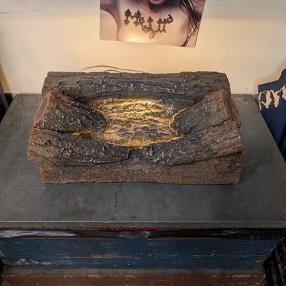A rustic, bark-textured rectangular planter or tray with a glowing yellow-orange crack-like pattern in the center, displayed on a dark table in an indoor setting.