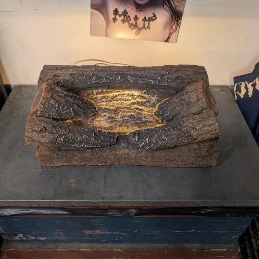A rustic, bark-textured rectangular planter or tray with a glowing yellow-orange crack-like pattern in the center, displayed on a dark table in an indoor setting.